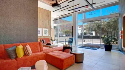 Welcoming lobby at The Linden Luxury Apartments with a bold orange sectional sofa, modern decor, and large windows for natural light.