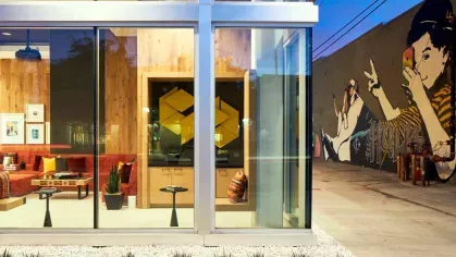 "View into the vibrant lounge area of The Linden Luxury Apartments through large glass windows, showcasing modern art and cozy red seating"