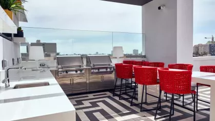 "Rooftop barbecue area at The Linden Luxury Apartments with sleek stainless steel grills, bold red seating, and panoramic city views"