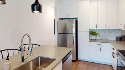Stylish kitchen with stainless steel appliances, white hexagonal backsplash tiles, and a spacious island with bar seating at The Prospector Modern Luxury Apartments.