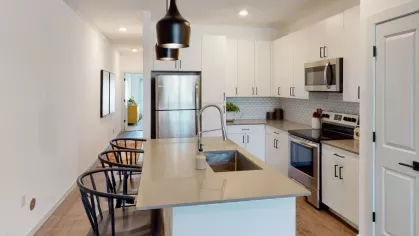 Stylish kitchen with stainless steel appliances, white hexagonal backsplash tiles, and a spacious island with bar seating at The Prospector Modern Luxury Apartments.