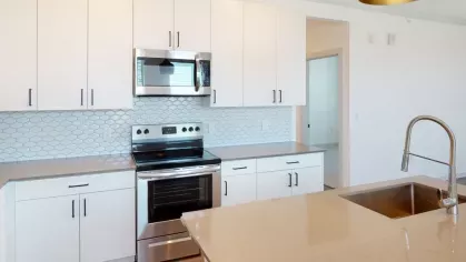 Elegant kitchen with quartz countertops, modern black pendant lighting, and a stainless steel refrigerator at The Prospector Modern Luxury Apartments.