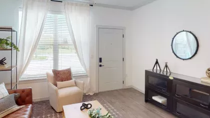 Cozy living room with a mix of modern and rustic decor, featuring a leather sofa, light armchair, wooden coffee table, and natural light filtering through white curtains.