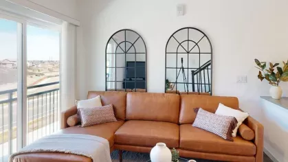 Bright and stylish living space with a caramel-colored sectional sofa, two arched mirrors, and access to a balcony with expansive views.