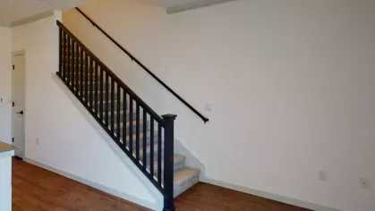 Open staircase with black railings and light wood flooring, leading to the upper level of the apartment.