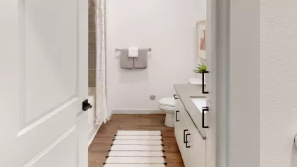 Elegant bathroom with white cabinetry, a long countertop, and a minimalist design with light wood flooring and a black-and-white striped runner.