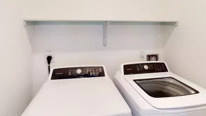 In-unit laundry area with high-efficiency washer and dryer, along with a practical overhead shelf for additional storage.