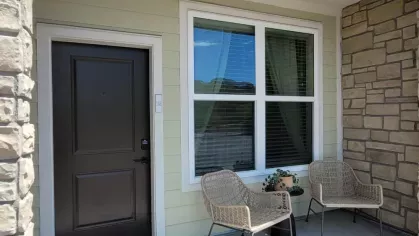Inviting apartment entryway with a charming patio, featuring two wicker chairs, a small plant, and a welcoming dark front door.