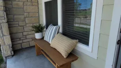 Welcoming outdoor patio with a wooden bench, decorative pillows, and a potted plant, creating a charming entryway vibe