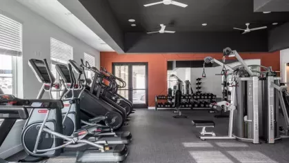 Well-equipped fitness room with a variety of cardio machines, weight training equipment, and a bold orange accent wall for a vibrant atmosphere.