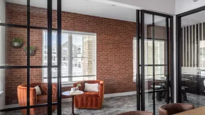 Cozy meeting or lounge space with exposed brick walls, plush orange chairs, and glass partitions for a blend of comfort and style.