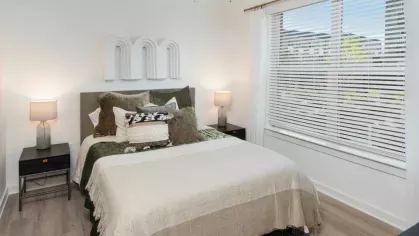 Bedroom with a neatly made bed, ceiling fan, and natural light streaming through the windows.