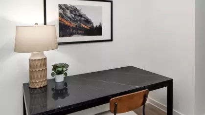A minimalist home office with a sleek black desk, a wooden chair, and framed mountain art on a white wall.
