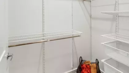 A spacious walk-in closet with white wire shelving and a woven basket with colorful throws.