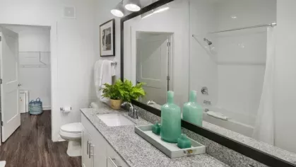 A modern bathroom with double sinks, granite countertops, and vibrant green accents against white cabinetry.