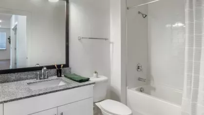 A bright bathroom with a simple white vanity, large mirror, and a shower-tub combo with a white curtain.