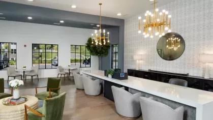 A stylish leasing office with a long white countertop, plush seating, and elegant gold chandeliers.