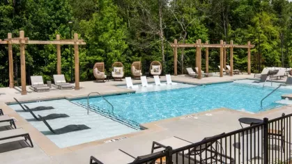 An inviting pool with lounge chairs, surrounded by lush trees and pergolas on a sunny day.