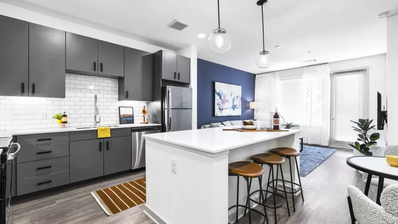 A modern kitchen with dark gray cabinetry, stainless steel appliances, and a large island with barstools, perfect for entertaining.