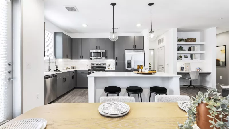 A stylish dining space with a wooden table set for a meal, seamlessly connected to a modern kitchen with pendant lighting and sleek finishes.