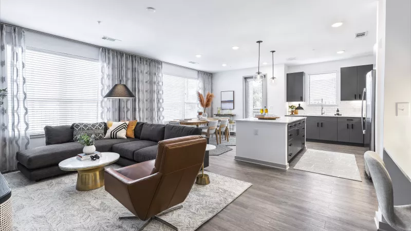 A cozy living area with a navy accent wall, a plush sectional, and a modern open-concept kitchen with sleek appliances and stylish pendant lighting.