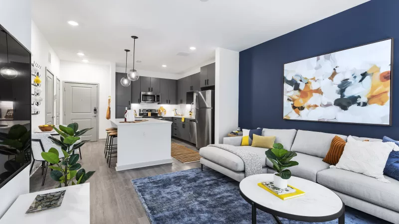 A cozy living area with a navy accent wall, a plush sectional, and a modern open-concept kitchen with sleek appliances and stylish pendant lighting.
