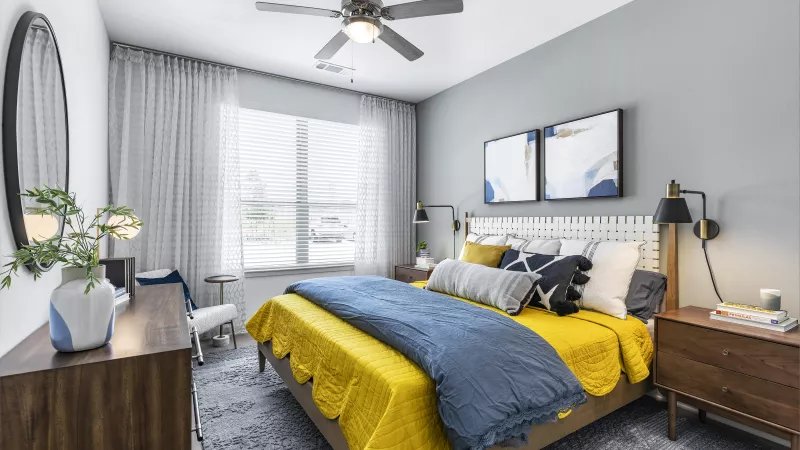 A trendy bedroom featuring a wooden bed frame, mustard and navy bedding, and decorative artwork above the headboard.