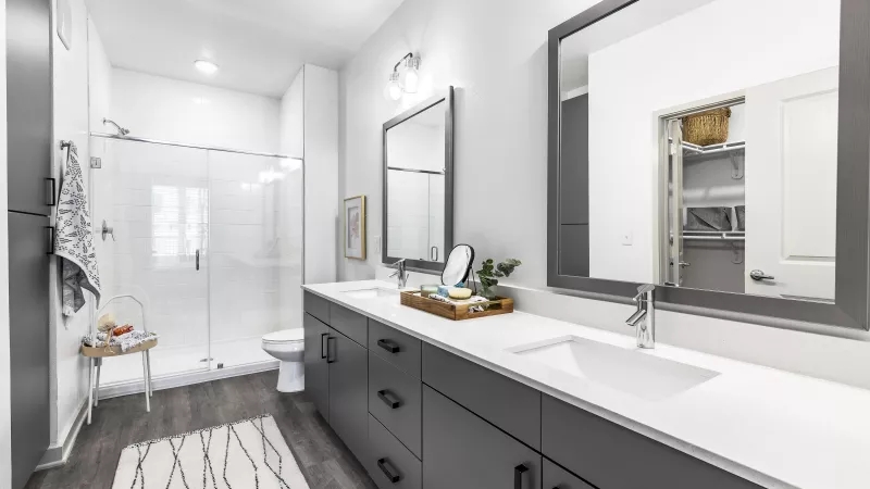 A sleek and spacious bathroom featuring a double vanity with modern fixtures, a glass-enclosed shower, and contemporary gray cabinetry.