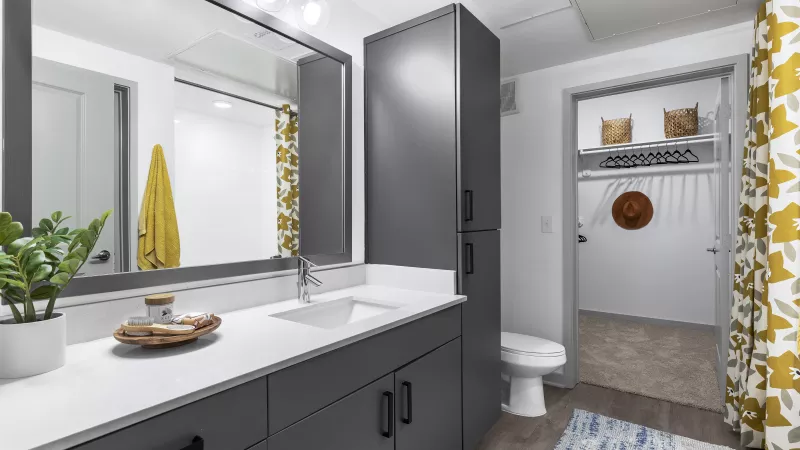 A spacious bathroom with a large vanity, a glass-enclosed shower, and a walk-in closet, designed with contemporary finishes and ample storage.