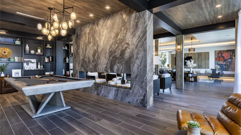 A luxurious entertainment space with a pool table, open shelving, and a double-sided fireplace that seamlessly connects the lounge and common area.