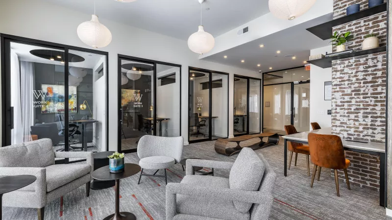A spacious community gathering space featuring warm wood accents, stylish seating, and floor-to-ceiling windows that enhance the open-concept design.