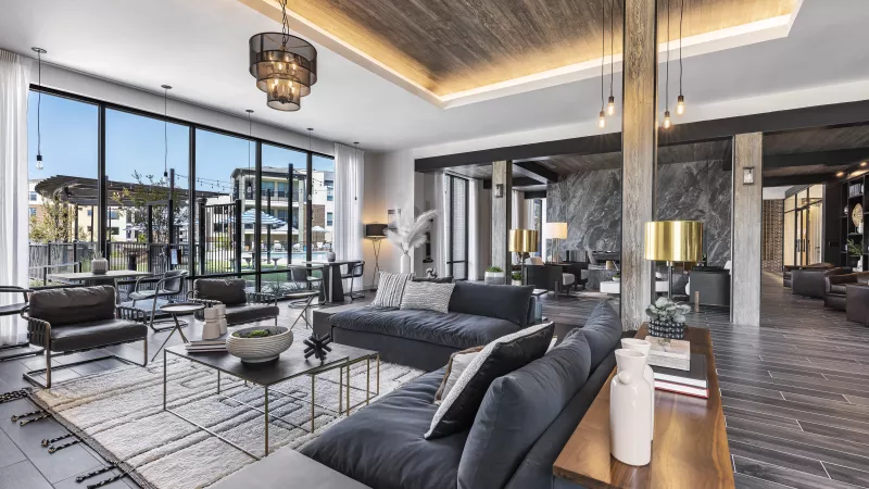 A spacious clubhouse at The Warner Apartments, featuring a striking wood ceiling, a large built-in media wall, and a modern, neutral-toned lounge area with contemporary décor.