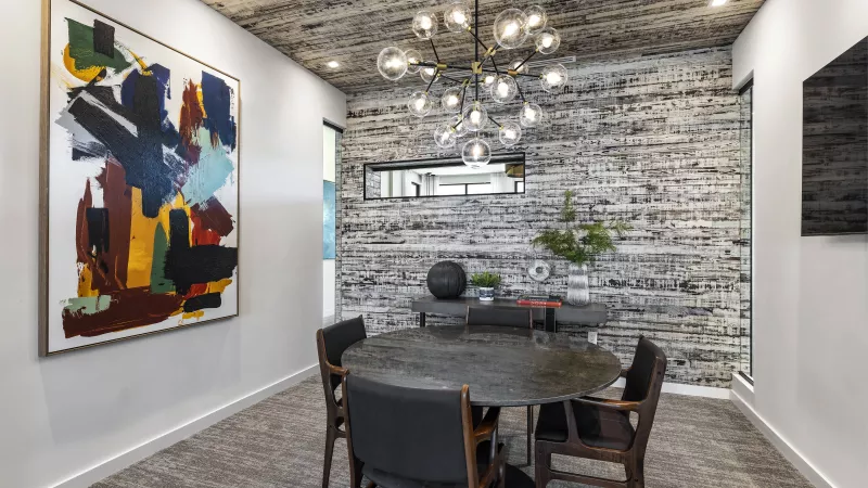 A sleek and modern conference room at The Warner Apartments featuring a glass partition, a statement chandelier, and a minimalist aesthetic, ideal for meetings or collaboration.