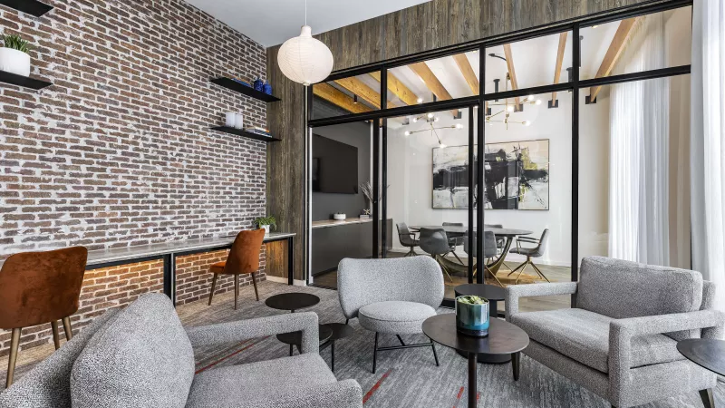 A modern and inviting lounge at The Warner Apartments featuring dark-toned sofas, a sleek coffee table, and built-in bookshelves with decorative accents, illuminated by stylish pendant lighting.