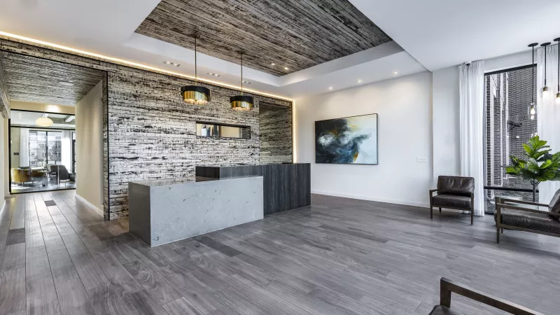A cozy seating area in The Warner Apartments' clubhouse with plush chairs, a modern fireplace set against a dramatic stone wall, and built-in bookshelves adding a touch of sophistication.