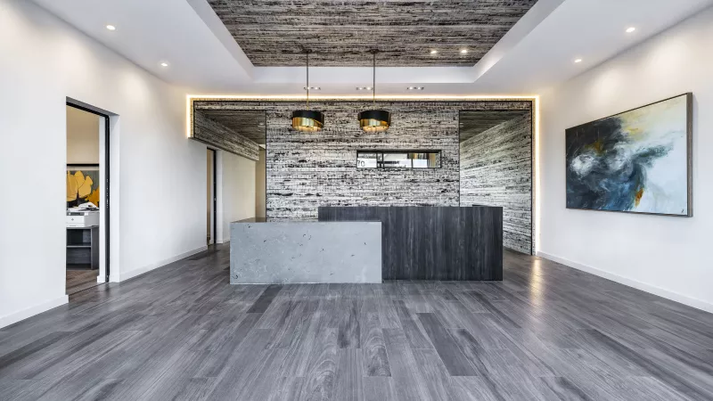 The reception area showcases a sleek concrete desk, textured wood walls, and contemporary lighting for a welcoming first impression.