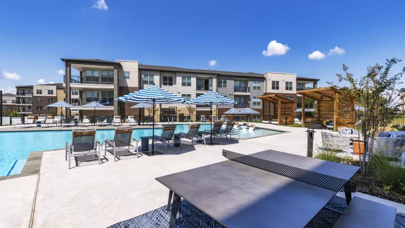 A shaded seating area with a modern ping-pong table overlooks the expansive resort-style pool and cabanas.