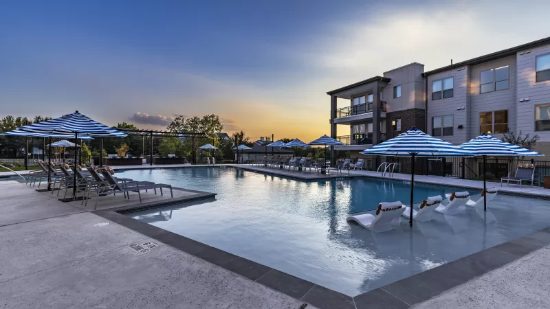 The shimmering pool reflects the soft hues of the sunset, with in-water loungers and striped umbrellas adding to the tranquil ambiance