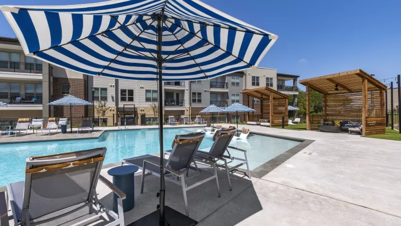Comfortable lounge chairs sit beneath blue-and-white striped umbrellas, offering a shaded retreat next to the sparkling swimming pool