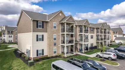 Exterior view of a three-story apartment building at Victoria Manor featuring private balconies and stone accents, with a spacious parking lot and landscaped grounds.