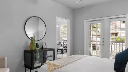 A serene bedroom with a white bed, ceiling fan, and double French doors leading to a balcony.