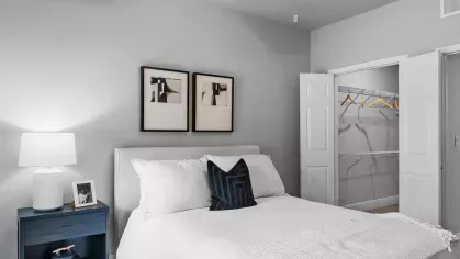 A cozy bedroom with a white bed, modern decor, and an open closet with hanging space.