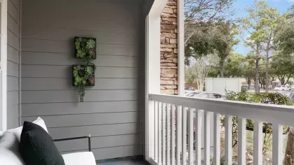 A charming balcony with a cozy white cushioned chair, decorative wall art, and a view of lush greenery.