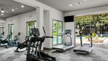 A well-equipped fitness center with treadmills, elliptical machines, and a view of the outdoor pool area.