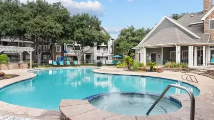 A serene pool with a stone-lined hot tub and a backdrop of charming apartment buildings.