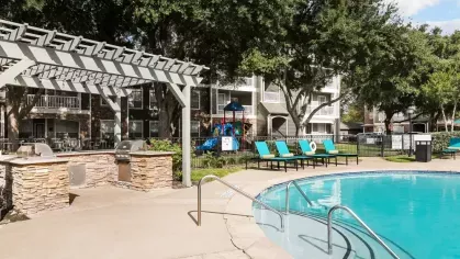 A pool area featuring a pergola, vibrant lounge chairs, and beautifully landscaped surroundings.