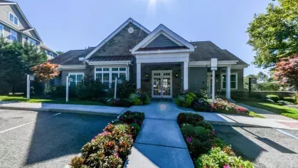 The leasing office at Vista at Town Green Luxury Apartments, featuring a charming stone and siding exterior with a welcoming entrance. The beautifully landscaped walkway is lined with vibrant flowers, creating an inviting atmosphere for residents and visitors.
