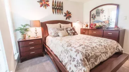 Beautifully furnished bedroom with a wooden bed frame, floral bedding, and charming decor accents at Forest Creek Apartments