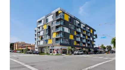 Modern exterior view of The Linden Luxury Apartments, featuring bold architecture with yellow and grey accents, spacious balconies, and prominent "Now Leasing" signage at the corner of 4th Street and Linden Avenue.