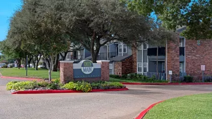 Community entrance sign for 1303 Main Apartments surrounded by trees and landscaping